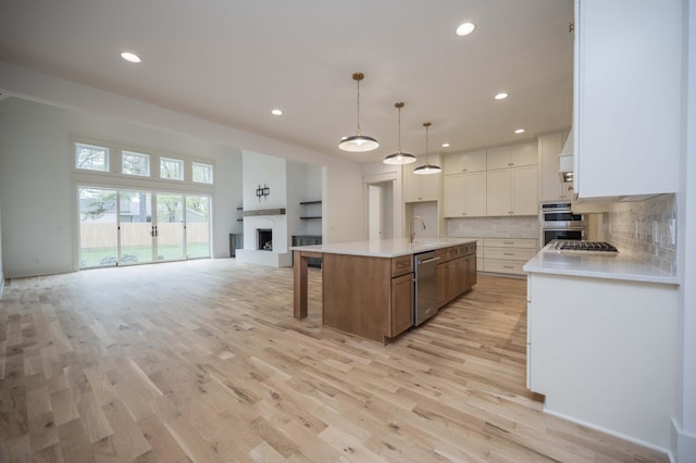 kitchen with pendant lighting, a center island with sink, decorative backsplash, appliances with stainless steel finishes, and white cabinetry