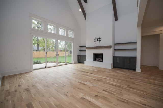 unfurnished living room with a fireplace, beam ceiling, a towering ceiling, and hardwood / wood-style floors