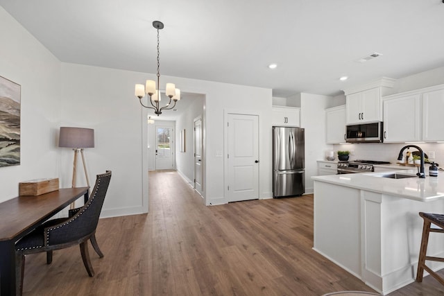 kitchen featuring sink, an inviting chandelier, appliances with stainless steel finishes, white cabinets, and hardwood / wood-style flooring