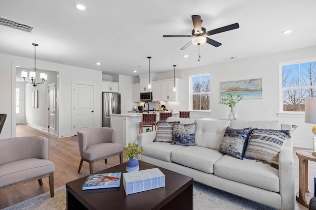 living room featuring ceiling fan with notable chandelier, sink, and light hardwood / wood-style flooring