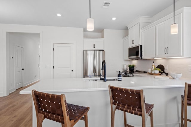 kitchen featuring a breakfast bar, decorative light fixtures, stainless steel appliances, and light hardwood / wood-style flooring