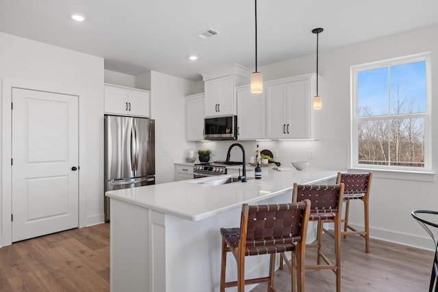 kitchen with kitchen peninsula, light wood-type flooring, decorative light fixtures, white cabinetry, and stainless steel appliances