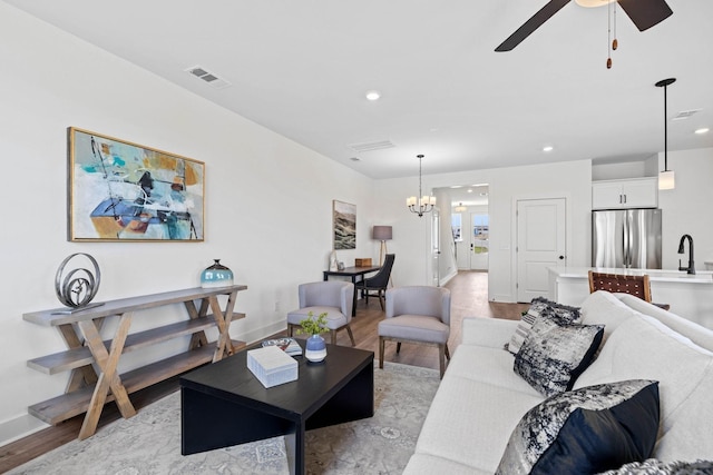 living room with ceiling fan with notable chandelier, light wood-type flooring, and sink