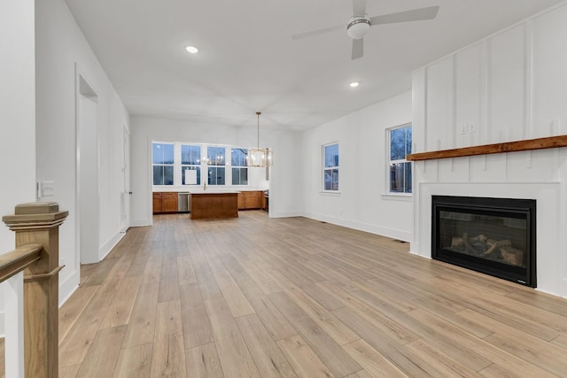 unfurnished living room featuring ceiling fan with notable chandelier, a large fireplace, and light hardwood / wood-style floors