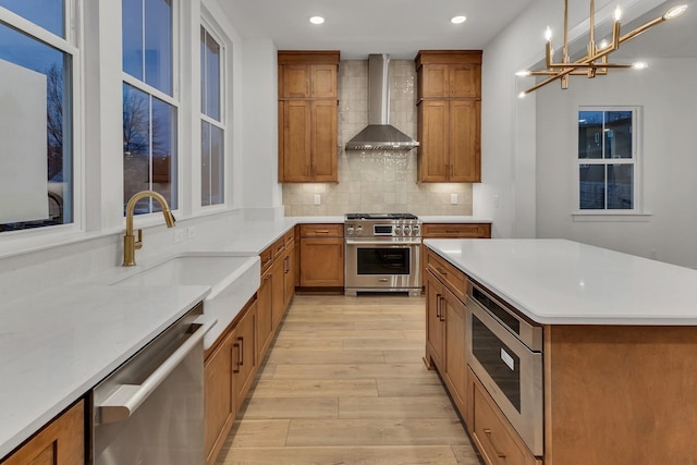 kitchen with wall chimney exhaust hood, hanging light fixtures, light wood-type flooring, stainless steel appliances, and backsplash