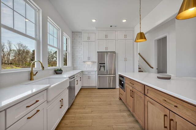 kitchen with appliances with stainless steel finishes, decorative light fixtures, sink, white cabinets, and backsplash