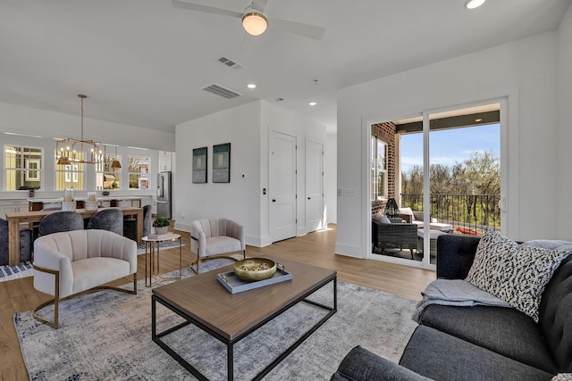 living room with ceiling fan with notable chandelier and light hardwood / wood-style flooring