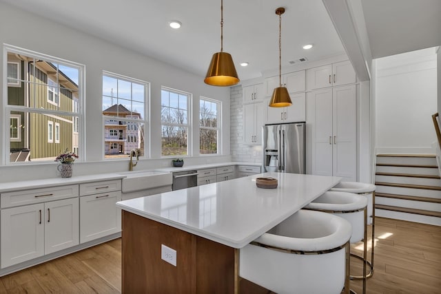 kitchen with stainless steel appliances, a kitchen island, hanging light fixtures, and white cabinets