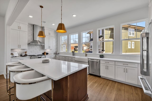 kitchen with stainless steel dishwasher, high quality fridge, a kitchen breakfast bar, wall chimney range hood, and white cabinets