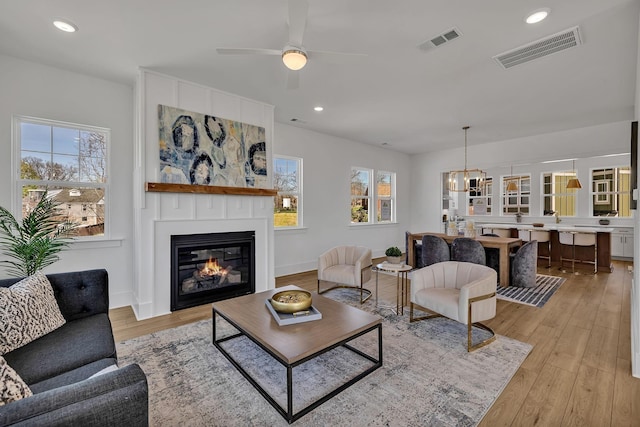 living room with ceiling fan, a large fireplace, and light wood-type flooring