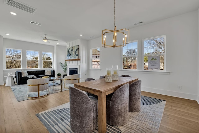 dining area with ceiling fan with notable chandelier and light hardwood / wood-style flooring