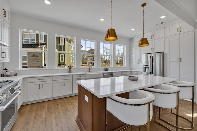 kitchen featuring a breakfast bar, premium appliances, white cabinets, a kitchen island, and decorative light fixtures