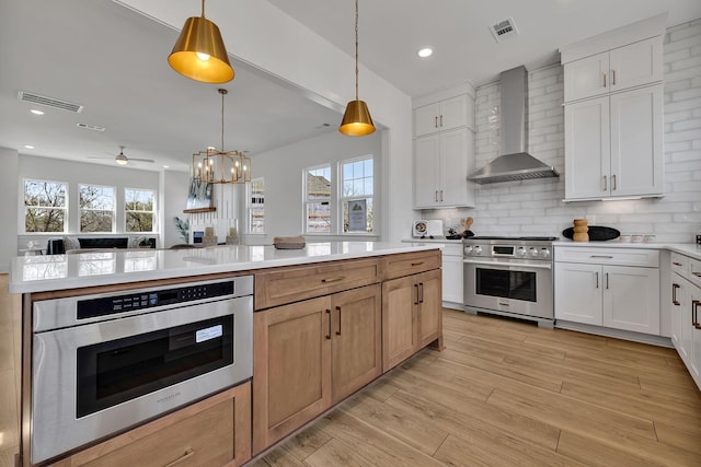 kitchen featuring white cabinetry, wall chimney range hood, stainless steel stove, and decorative light fixtures