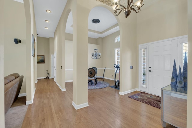 entryway featuring light hardwood / wood-style floors, a towering ceiling, a tray ceiling, and an inviting chandelier