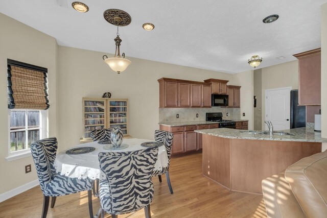 kitchen with light stone countertops, sink, light hardwood / wood-style flooring, kitchen peninsula, and black appliances