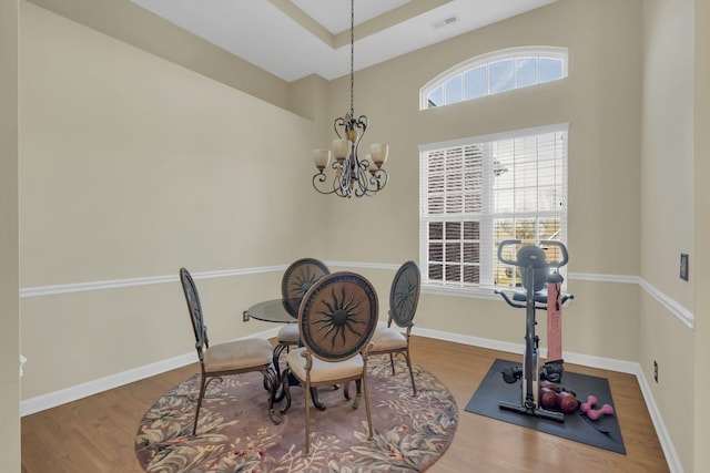 dining area with wood-type flooring, a tray ceiling, and a notable chandelier