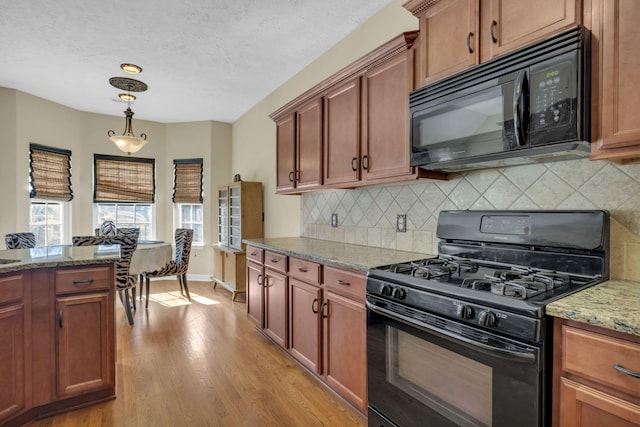 kitchen featuring light stone counters, pendant lighting, decorative backsplash, black appliances, and light wood-type flooring