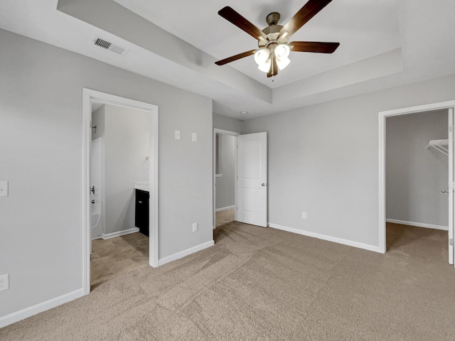 unfurnished bedroom with light carpet, a tray ceiling, ceiling fan, a spacious closet, and a closet