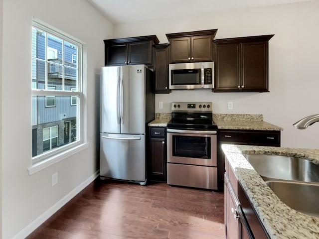 kitchen featuring dark brown cabinetry, sink, light stone counters, dark hardwood / wood-style floors, and appliances with stainless steel finishes