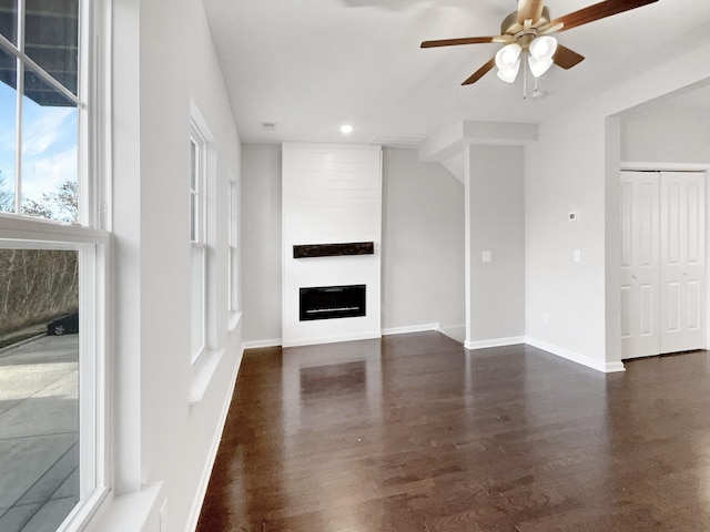 unfurnished living room featuring dark hardwood / wood-style flooring, ceiling fan, and a large fireplace