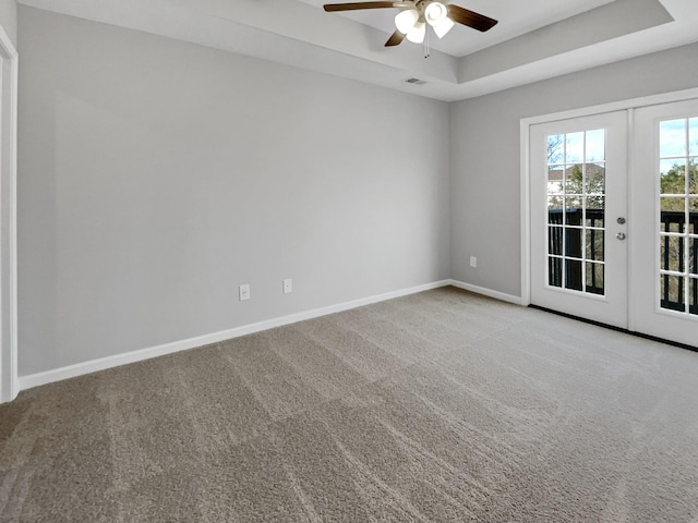 carpeted empty room featuring ceiling fan, a tray ceiling, and french doors