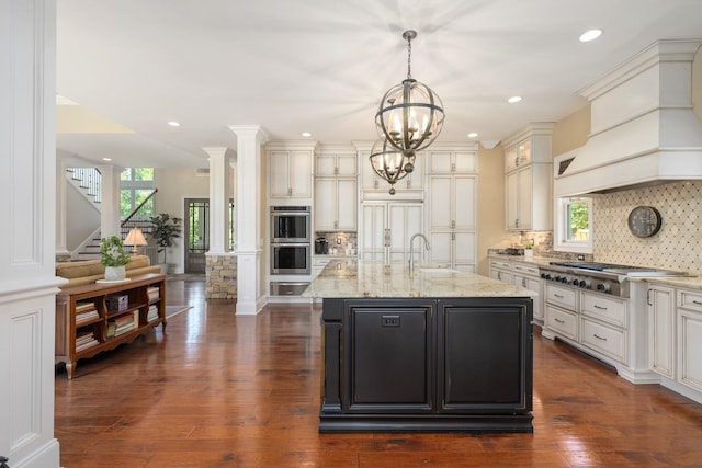 kitchen featuring a center island with sink, backsplash, custom range hood, and stainless steel appliances