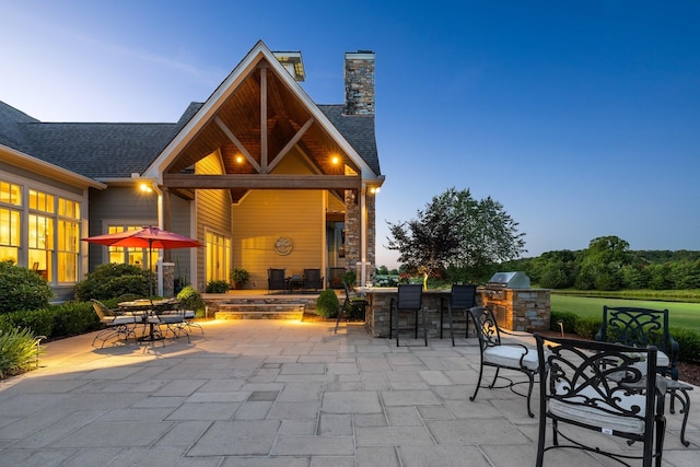 patio terrace at dusk featuring an outdoor kitchen and an outdoor bar