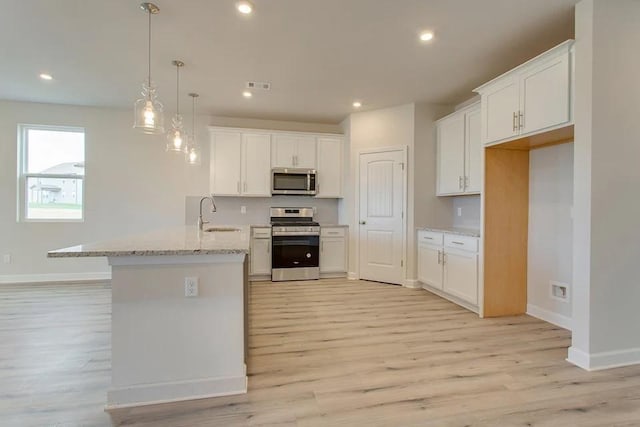 kitchen with light stone countertops, appliances with stainless steel finishes, light wood-type flooring, and white cabinetry