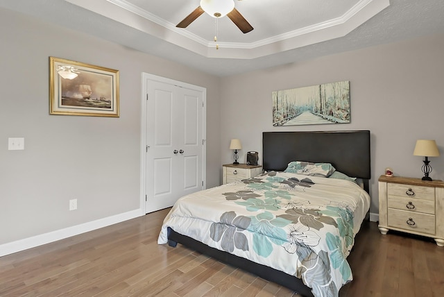 bedroom featuring a raised ceiling, a closet, ceiling fan, and crown molding