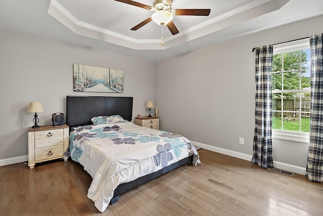 bedroom with a raised ceiling, multiple windows, ceiling fan, and hardwood / wood-style floors