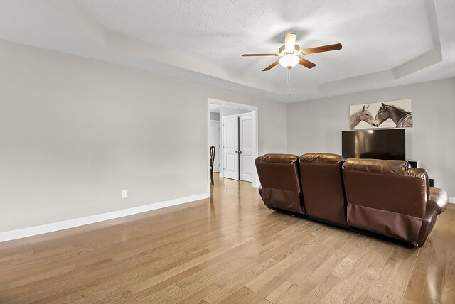 living room featuring ceiling fan, light wood-type flooring, a textured ceiling, and a tray ceiling