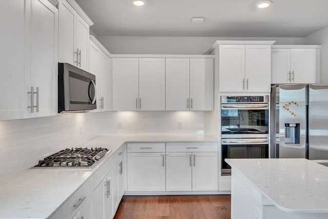 kitchen featuring backsplash, white cabinetry, wood-type flooring, and appliances with stainless steel finishes