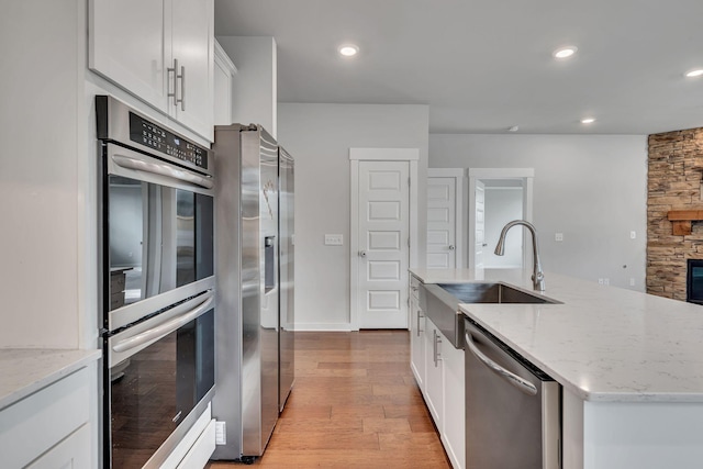 kitchen featuring appliances with stainless steel finishes, light wood-type flooring, sink, white cabinetry, and an island with sink