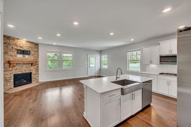 kitchen with a stone fireplace, a kitchen island with sink, white cabinets, and stainless steel appliances