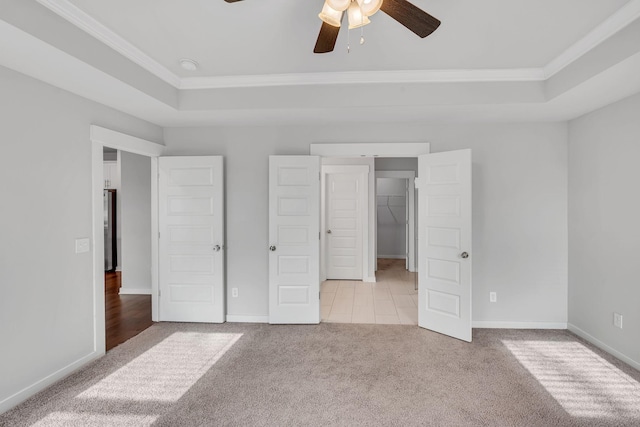 unfurnished bedroom featuring ceiling fan, light colored carpet, a walk in closet, and a tray ceiling