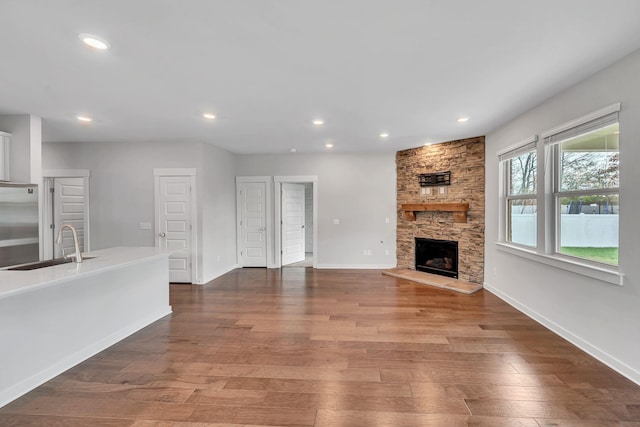 unfurnished living room with hardwood / wood-style floors, a stone fireplace, and sink