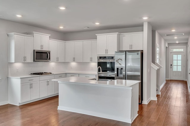 kitchen featuring white cabinets, a center island with sink, sink, appliances with stainless steel finishes, and wood-type flooring