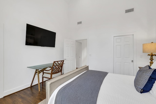 bedroom featuring a towering ceiling and dark wood-type flooring