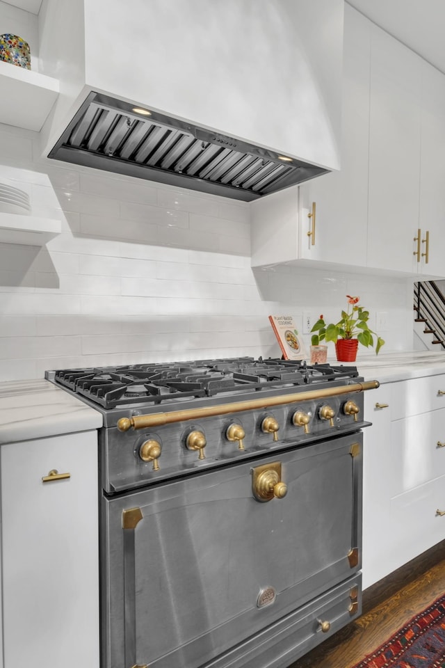 kitchen with high end stove, backsplash, white cabinetry, and range hood