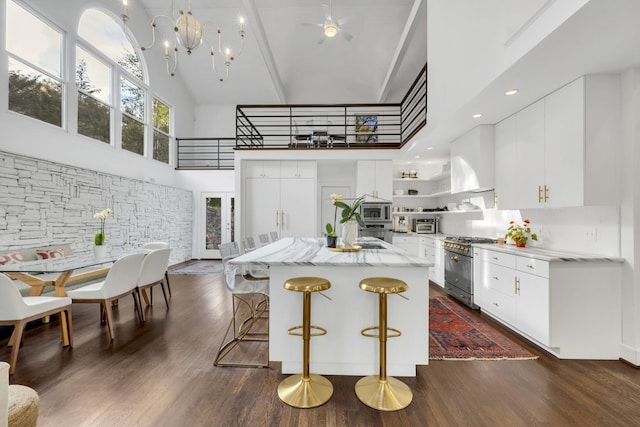 kitchen with a kitchen island, a towering ceiling, stainless steel appliances, and white cabinetry