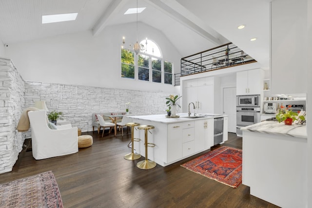 kitchen featuring a center island with sink, a skylight, appliances with stainless steel finishes, beam ceiling, and white cabinetry