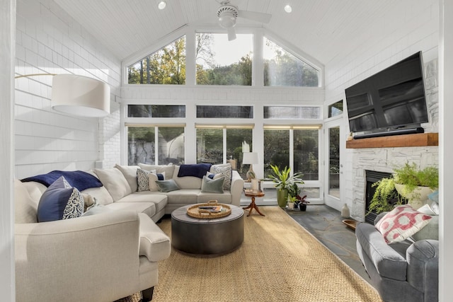 sunroom featuring a wealth of natural light, wood ceiling, vaulted ceiling, ceiling fan, and a stone fireplace