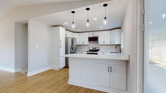 kitchen featuring white cabinets, hanging light fixtures, appliances with stainless steel finishes, light hardwood / wood-style floors, and kitchen peninsula