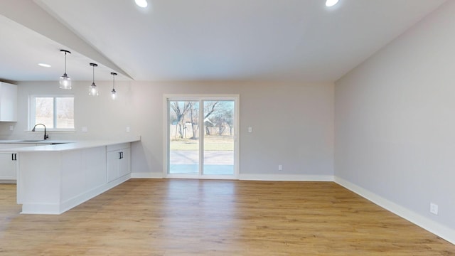 interior space with white cabinets, light wood-type flooring, decorative light fixtures, and a healthy amount of sunlight