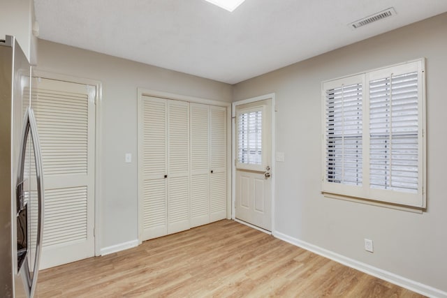 unfurnished bedroom with stainless steel fridge, light wood-type flooring, and two closets