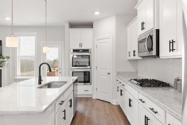 kitchen with light stone countertops, stainless steel appliances, a kitchen island with sink, sink, and pendant lighting