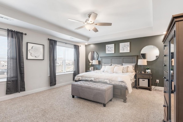 carpeted bedroom with a raised ceiling and ceiling fan