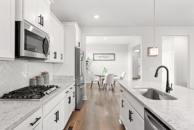 kitchen featuring light stone countertops, stainless steel appliances, sink, pendant lighting, and white cabinets