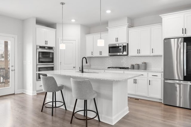 kitchen with appliances with stainless steel finishes, an island with sink, hanging light fixtures, and sink