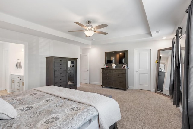 carpeted bedroom featuring a raised ceiling, ceiling fan, and ensuite bathroom